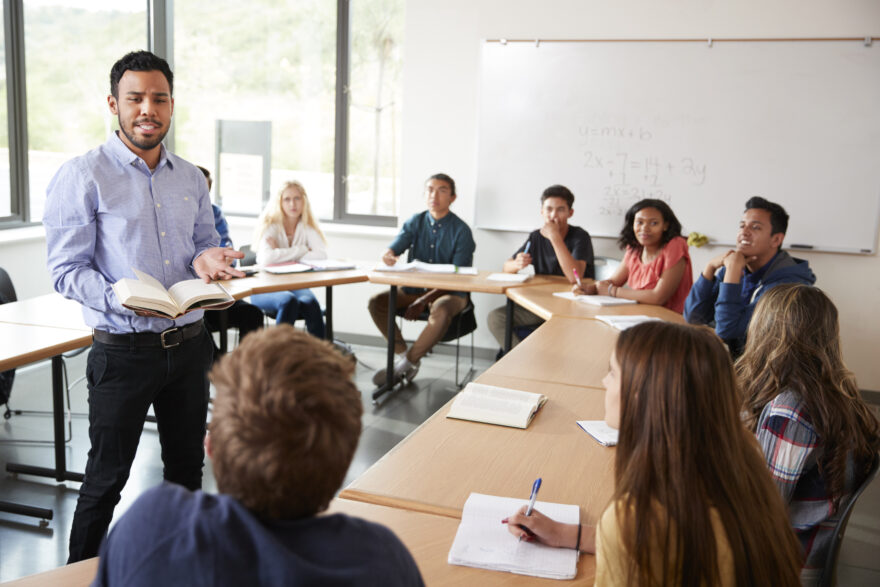 A group of students seated around a round table, with one person in the center leading a discussion about a business course.